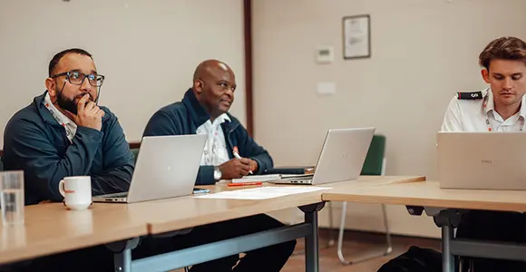 Candidates in a class with laptops looking ahead attentively.