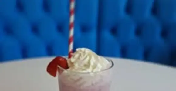 Strawberry milkshake topped with whipped cream and a strawberry, served in a tall glass on a café table.