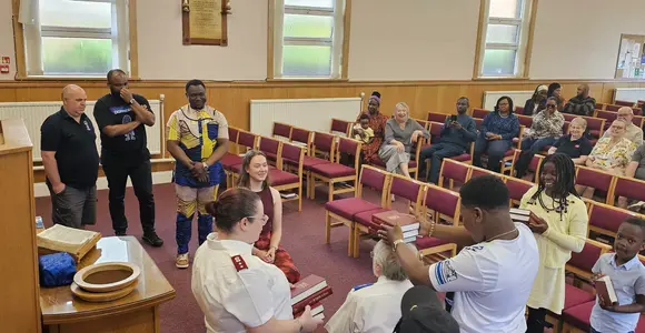 Parkhead Salvation Army church service. Many people can be seen including the Corps Officer and children and adults, taking part in a challenge in the main worship hall during a service.
