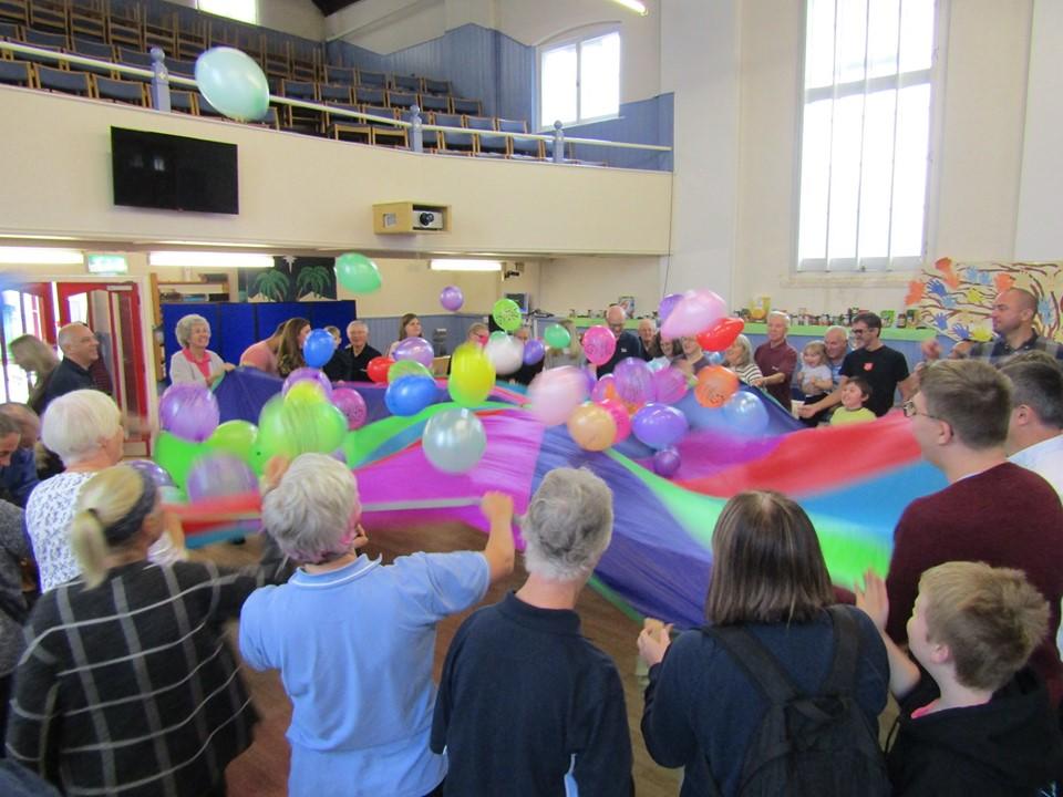 Our vibrant church goers all holding edges of a parachute bouncing balloons above head height