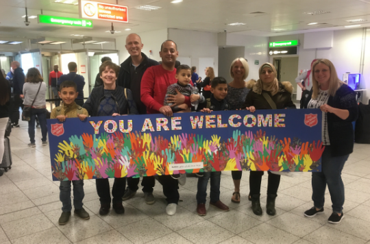 A group of people in an airport holding a sign that reads: You are welcome