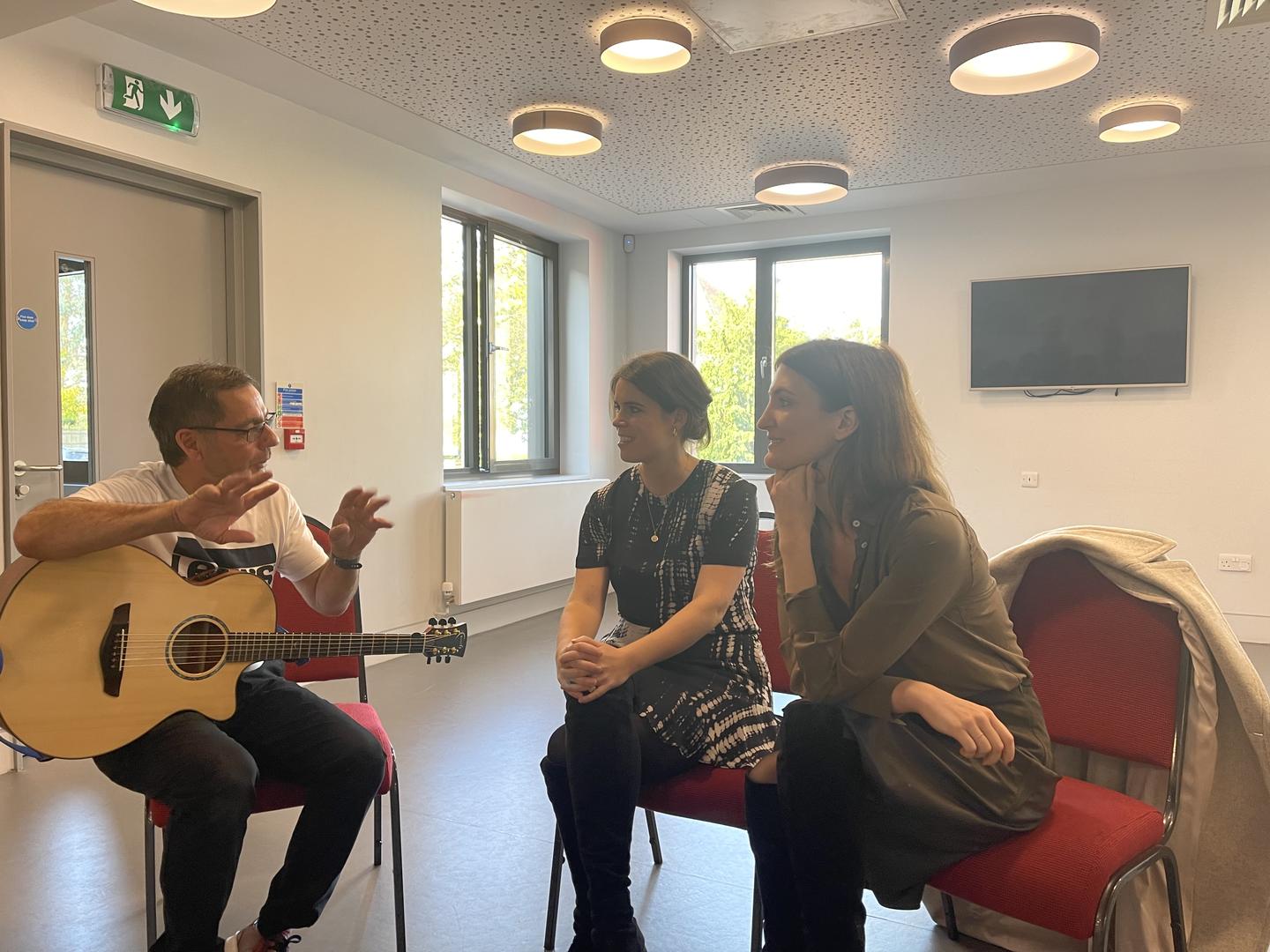 HRH Princess Eugenie and Julia de Boinville, Co-Founders of The Anti-Slavery Collective speak to specialist support worker Nigel Long, who holds a guitar.