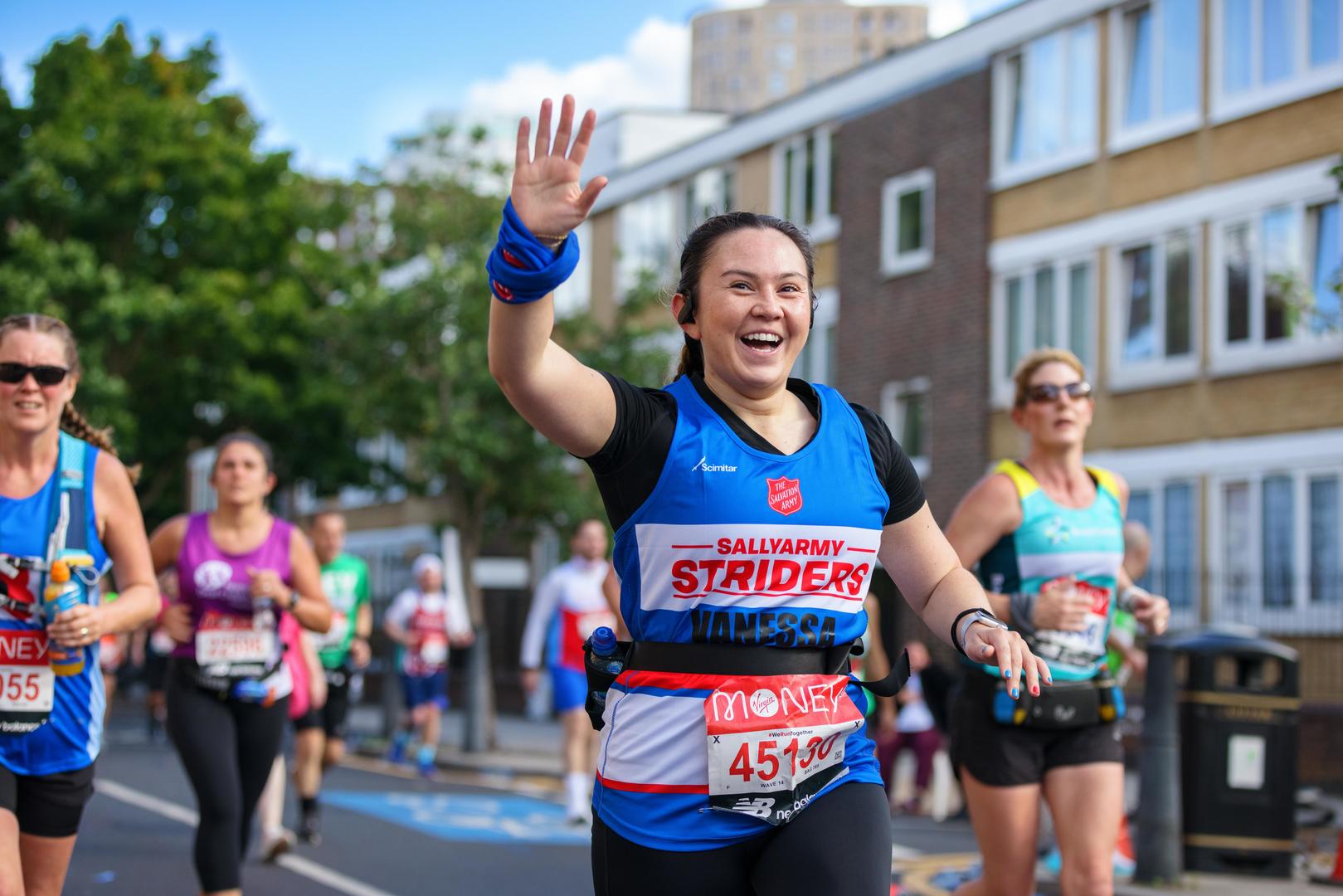 A woman smiling and waving at the camera as she runs the London Marathon to raise money for our homelessness services