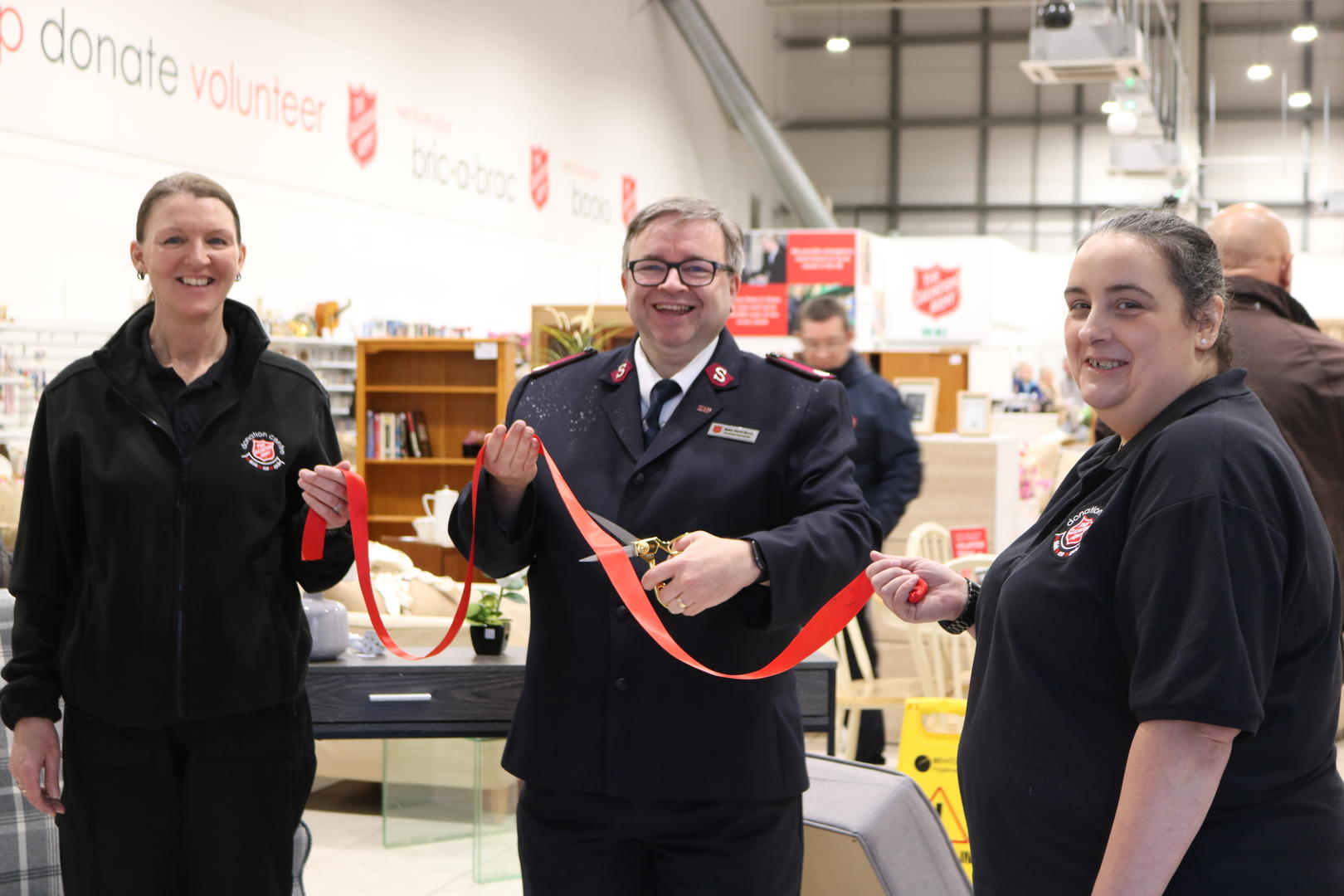 Two other Salvation Army staff members hold a ribbon whilst Sunderland's Divisional Commander cuts it to mark the opening of a new donation centre