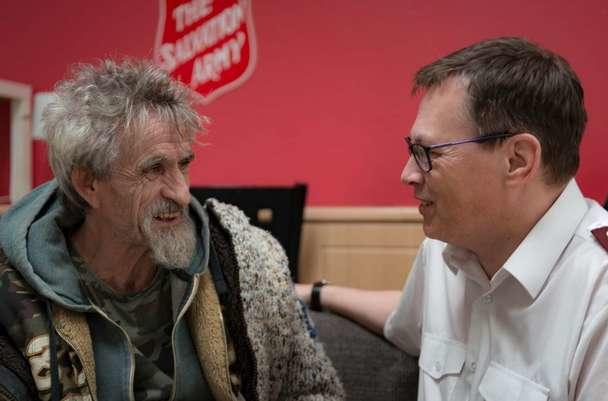 A Salvation Army Officer sitting and speaking with an older gentleman with a long silver beard.