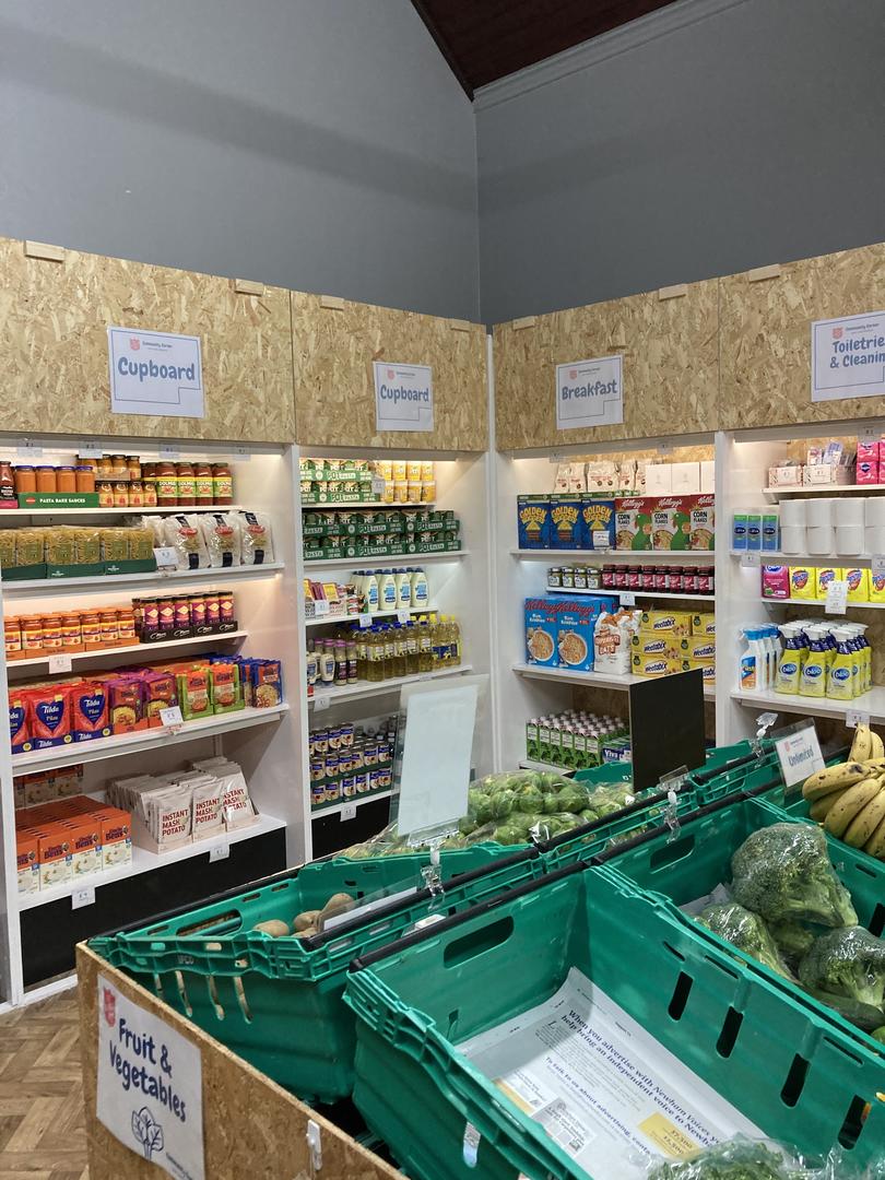 Image shows baskets for food and shelves full of food in a space that looks like a small supermarket.