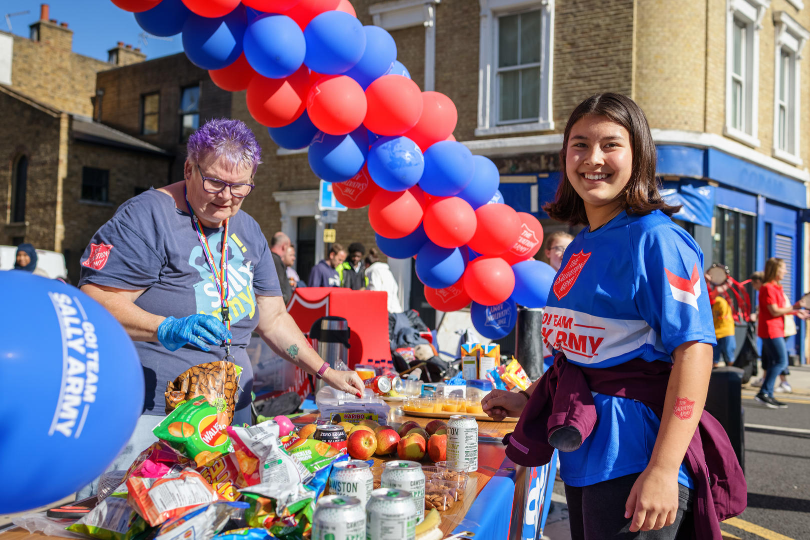 A smiling girl wearing a Salvation Army t-shirt helps to hand out food to runners at the London Marathon