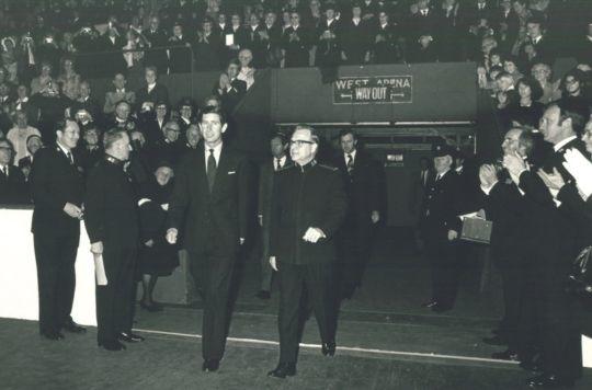 Prince Charles walks into an arena alongside a Salvation Army staff member at the 1978 International Congress, with crowds in the stands behind them.