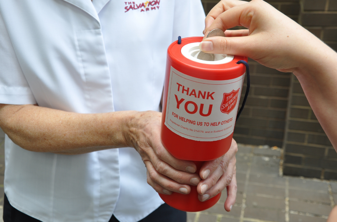 An image of someone putting money into a Salvation Army collection tin. 