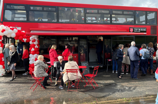 People sat outside the double decker red bus eating and drinking