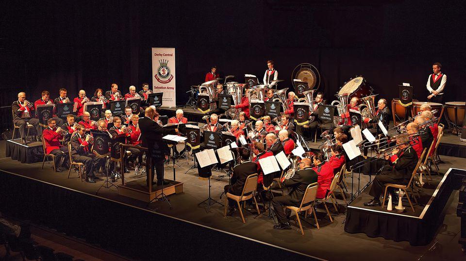 Two brass bands sitting down playing at a concert.