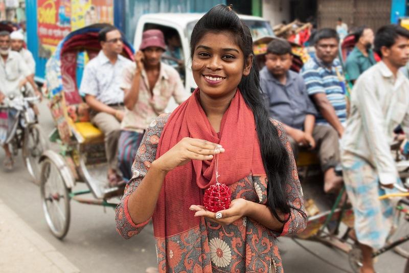 A Bangladeshi woman stands in the street smiling at the camera, holding one of the Christmas decorations and smiling at the camera. 