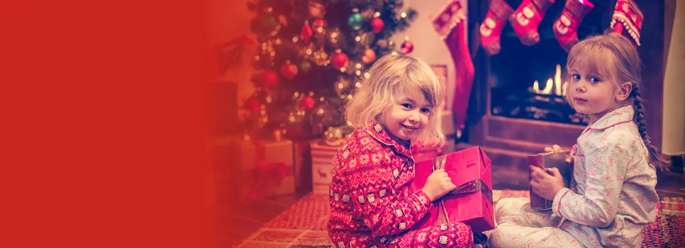 Two children sat with Christmas presents in front of fire