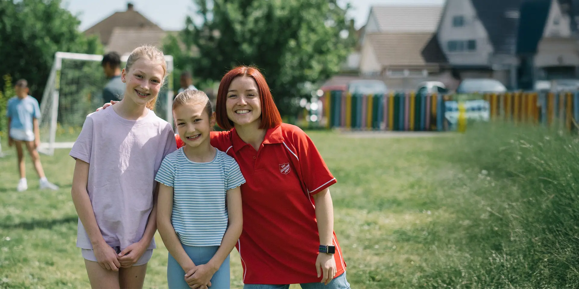 A salvation army staff member smiling alongside two children on a sports field