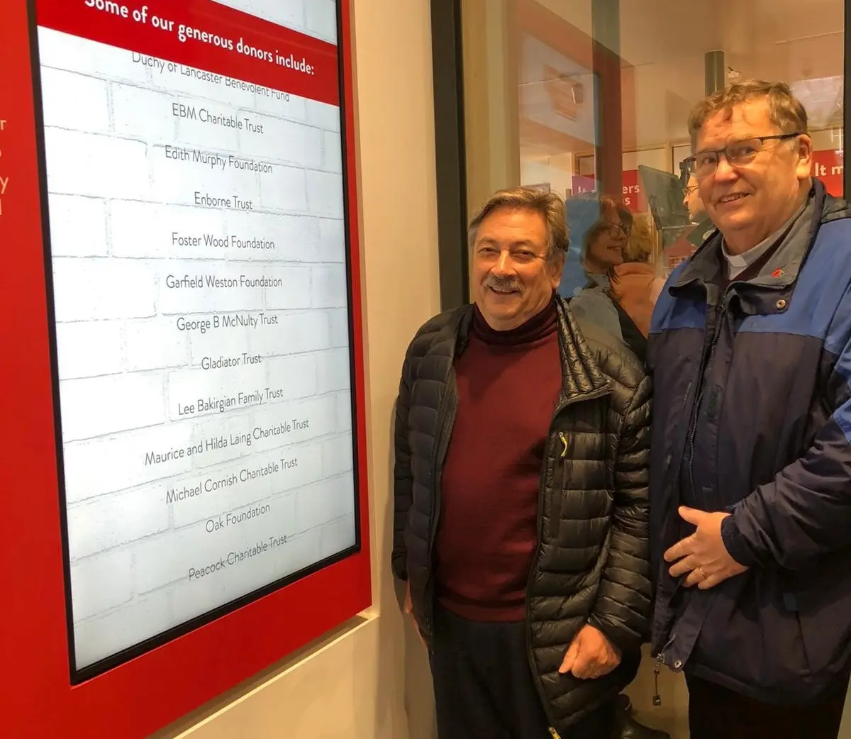 Two men smiling next to a sign for Strawberry Fields