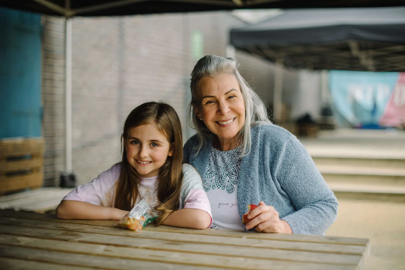 Woman sitting with young girl smiling at the camera, on a picnic table