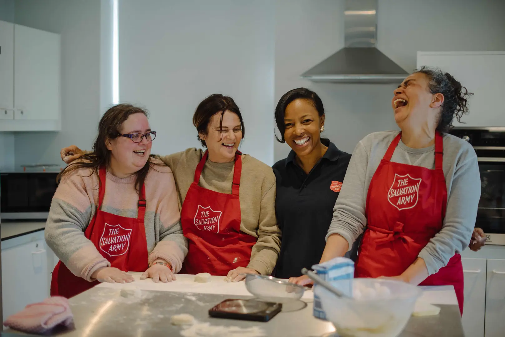 Four ladies wearing Salvation Army aprons in a kitchen smiling.