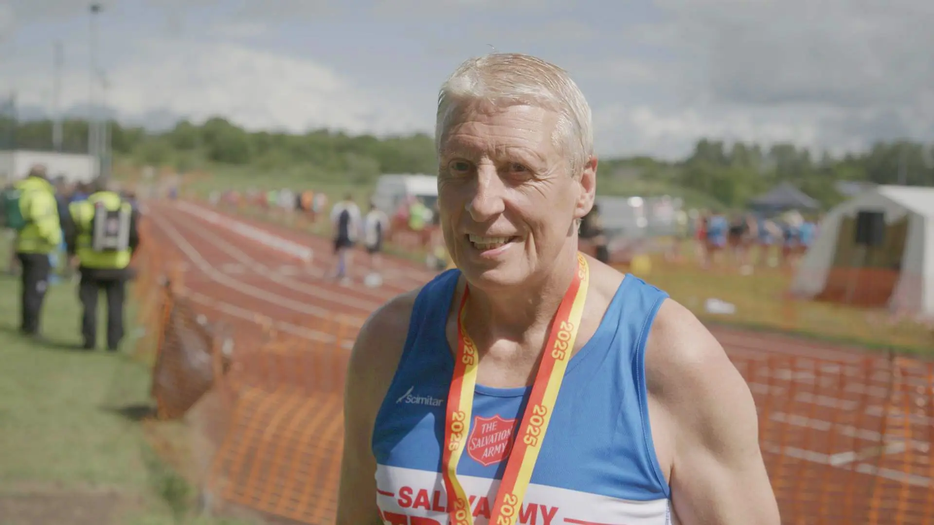 Marathon running man, at a race track, smiling at the camera. 