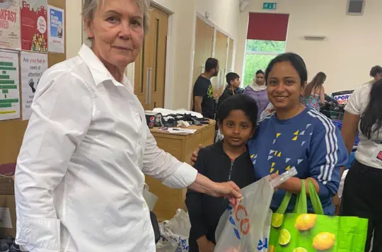 A woman hands a bag of items to a woman and child 