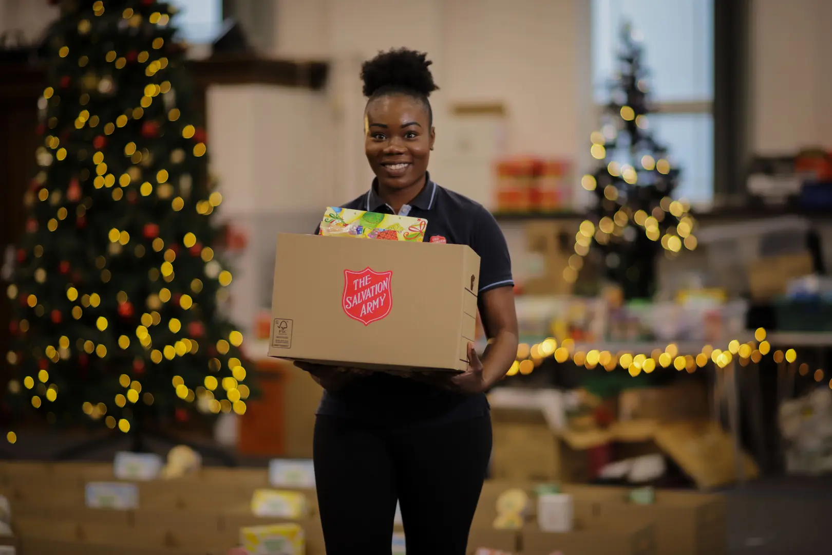 Person in TSA uniform standing with a cardboard box full of food with Christmas trees in the background