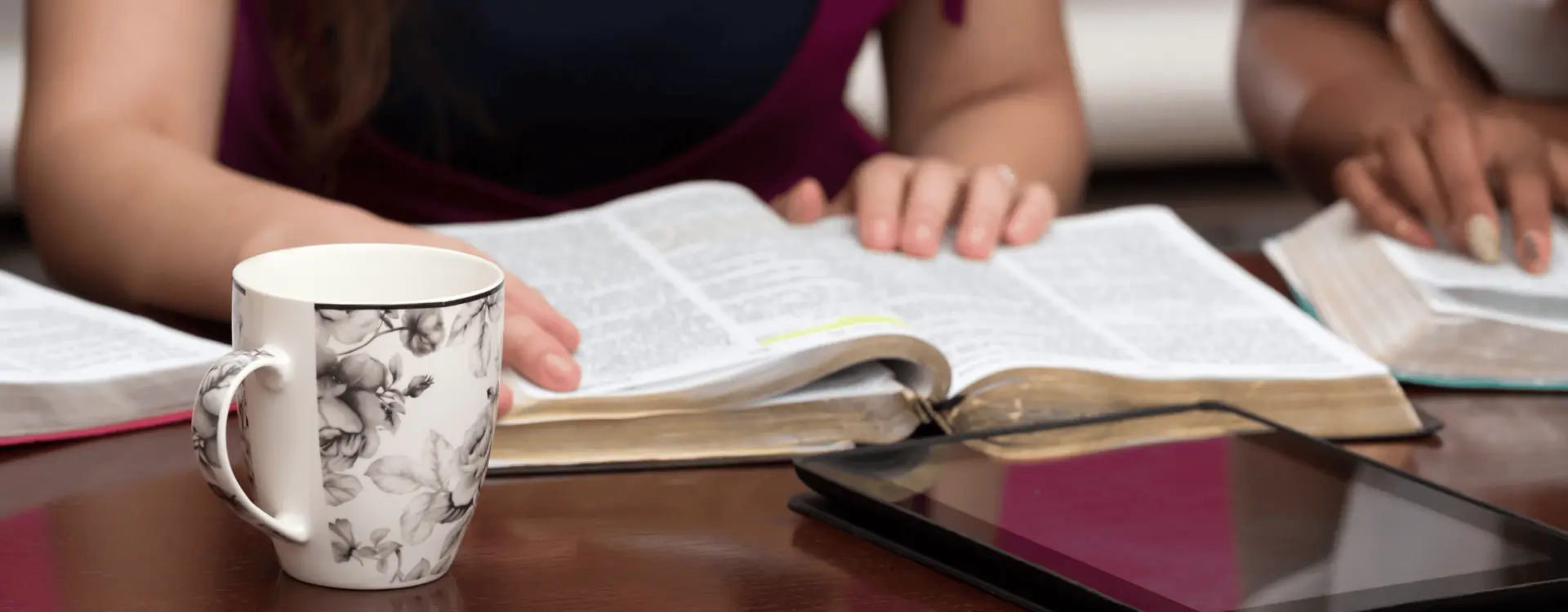 Woman reading a bible with a mug and ipad on table