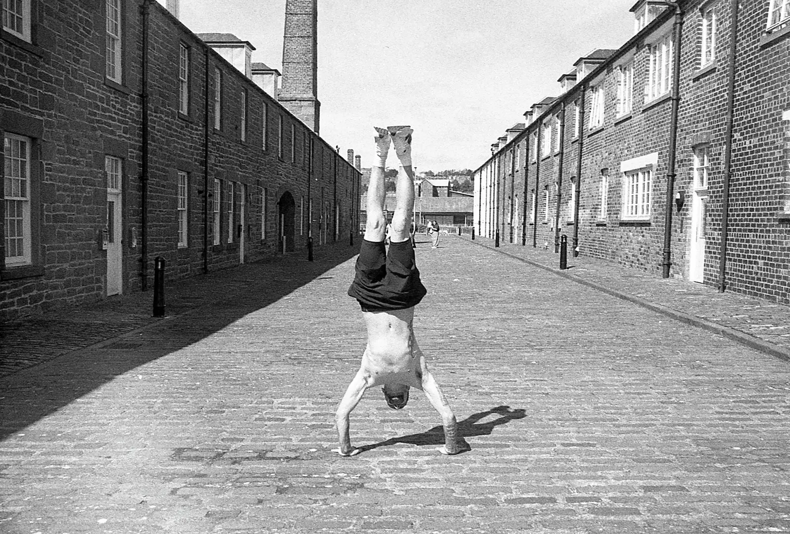 A man standing on his head in an old fashioned street in black and white