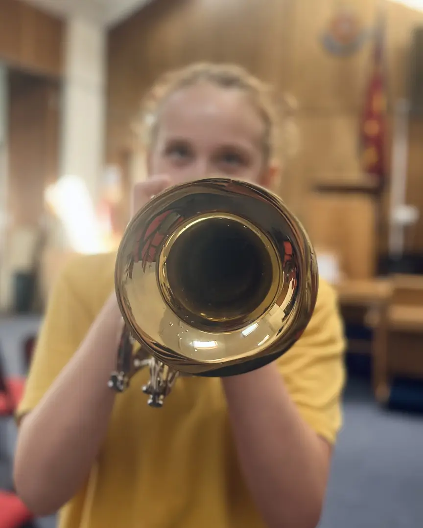 A young brass instrument leans forward, the instrument bell is in focus and The Salvation Army crest is in the background