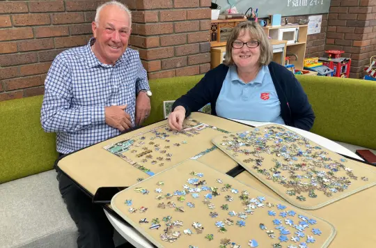 Picture of two people smiling at the camera doing a jigsaw 