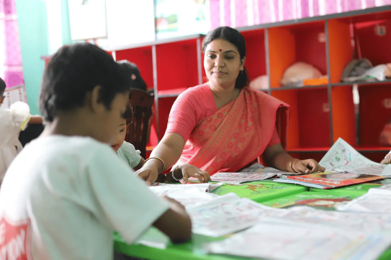 A teacher helps children with colourful activity sheets at a classroom table
