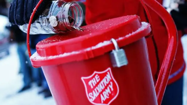 A red bucket with a Salvation Army shield on the side, with a collection of coins being poured into the top.
