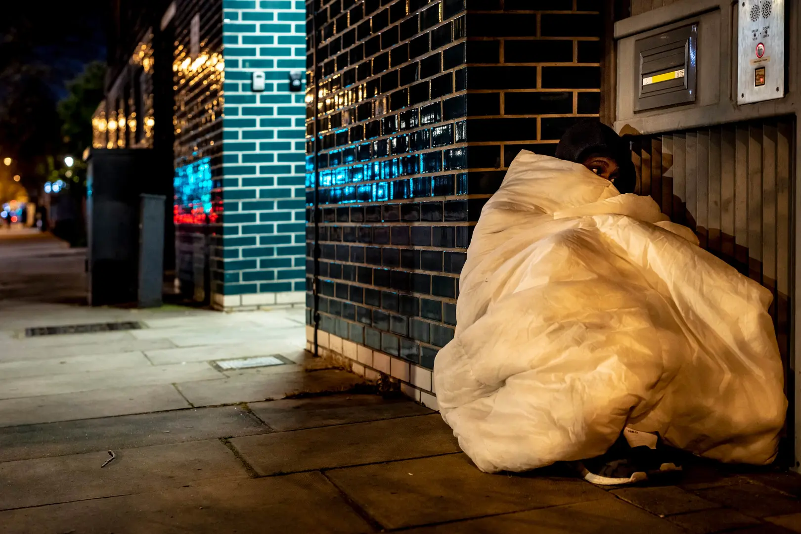 Homeless man on street corner wrapped in a duvet.