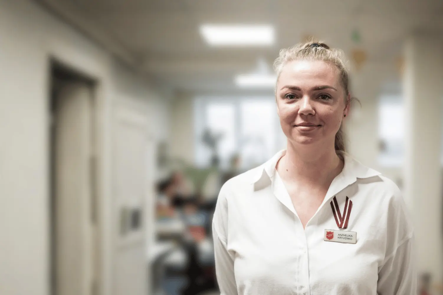 A woman wearing a white shirt and Salvation Army name badge stands facing the camera