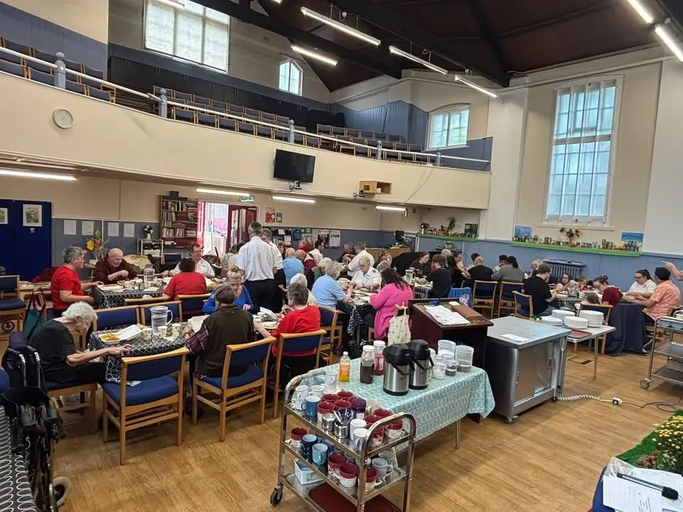 Congregation sitting around tables eating a lunch in Hove Salvation Army hall after Harvest Festival