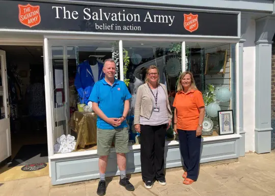 A picture of three people stood in front of a Salvation Army shop 