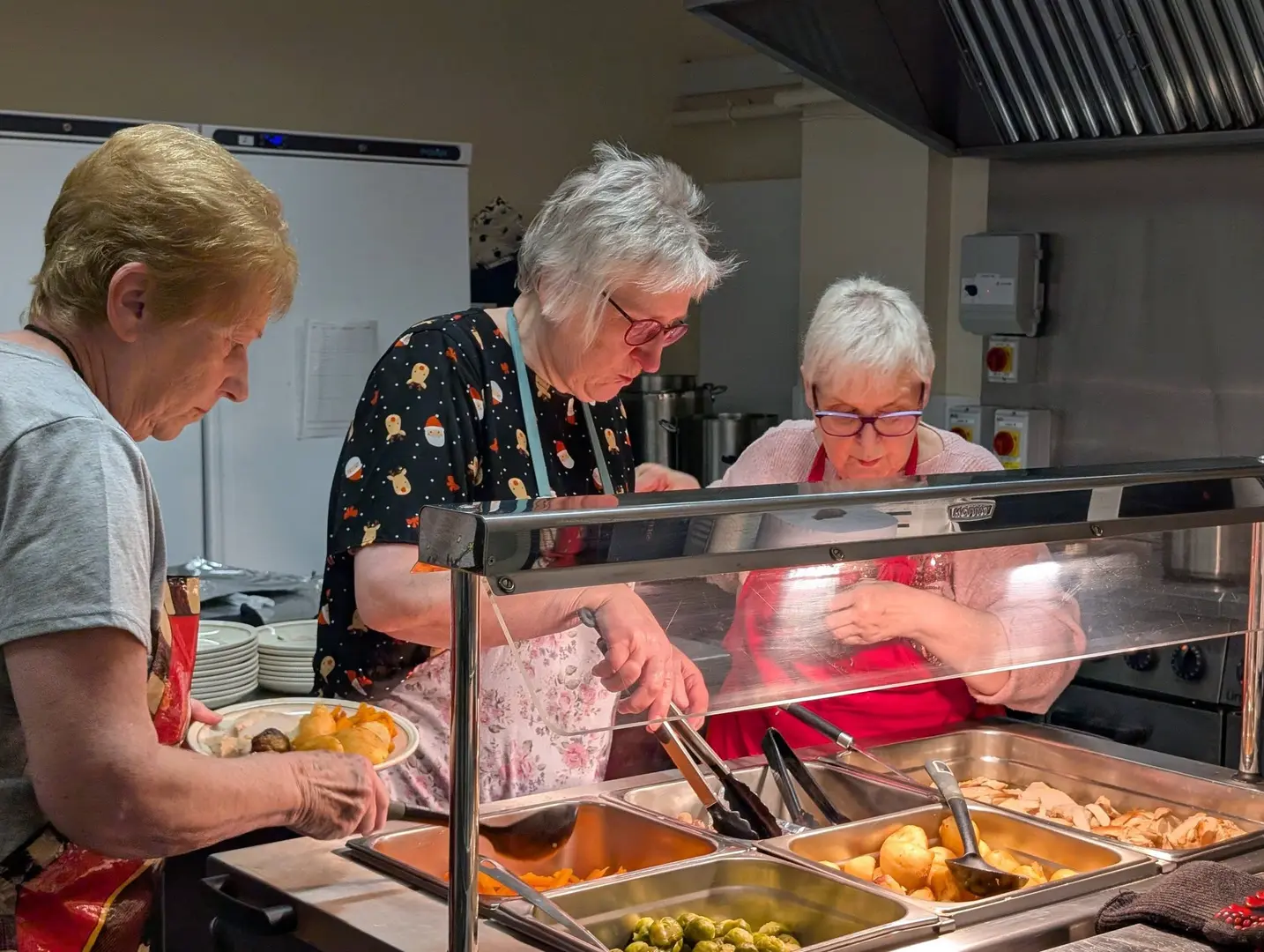Three ladies standing in the kitchen, serving Christmas dinner through the hatch.